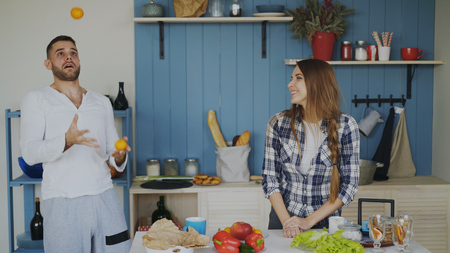 Attractive loving couple having fun in the kitchen. Handsome man juggle with fruits to impress his girlfriendの写真素材