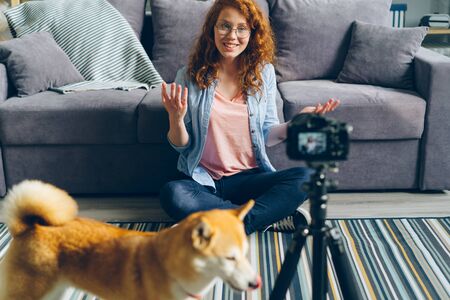 Cute teenager popular blogger is recording videoblog sitting on floor at home, stroking lovely pet dog and talking to subscribers. Social media and people concept.の写真素材