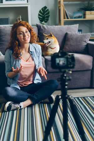 Happy girl creative vlogger recording video with adorable dog at home sitting on floor talking stroking cute pet. Social media and blogging concept.の写真素材