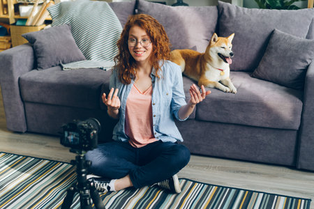 Female vlogger attractive young lady recording video at home with cute dog sitting on floor in...