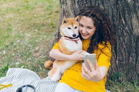 Portrait of happy young girl taking selfie with adorable dog in park hugging lovely pet holding camera smiling enjoying friendship with puppy. Youth and lifestyle concept.の写真素材