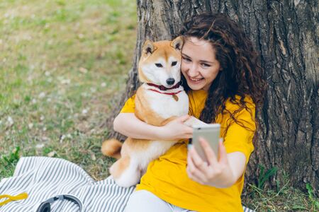 Portrait of happy young girl taking selfie with adorable dog in park hugging lovely pet holding camera smiling enjoying friendship with puppy. Youth and lifestyle concept.