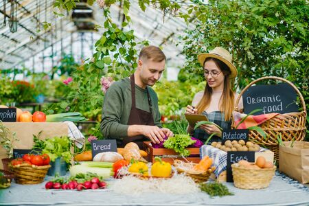 Cheerful young people farmers are putting organic food on table at farm sales talking smiling writing in notebook. Youth, small business and agriculture concept.の写真素材