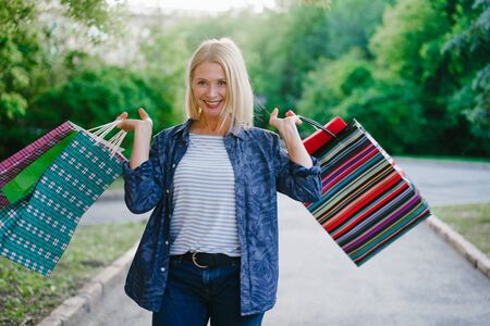Portrait of happy woman shopaholic standing outdoors with shopping bags smiling enjoying day in city park. Consumerism, happiness and lifestyle concept.の写真素材