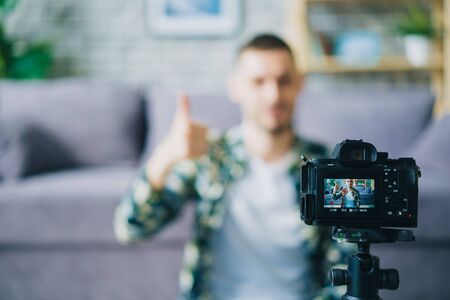 Close-up of digital camera recording modern blogger showing thumbs-up recording video in apartment, focus on equipment. People, technology and house concept.の写真素材