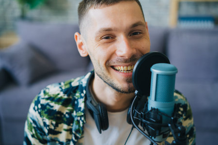 Portrait of joyful guy hipster talking in microphone in recording studio smiling looking at camera...