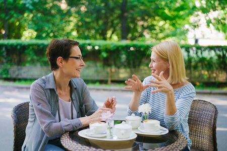 Beautiful mature ladies friends are talking sitting in street cafe together enjoying conversation. People, modern lifestyle and female friendship concept.の写真素材