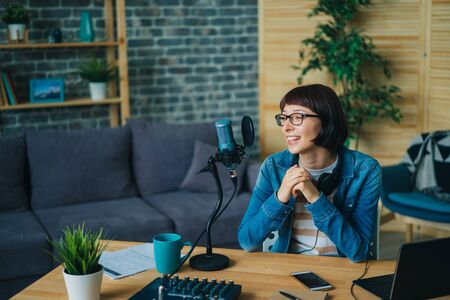 Happy girl blogger is speaking in microphone in recording studio smiling creating podcast for internet blog. Occupation, blogging and youth concept.の写真素材