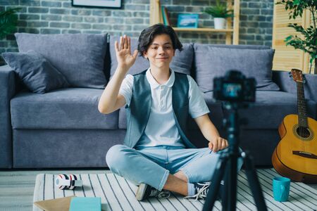 Joyful teenage boy speaking smiling gesturing in front of camera at home recording video for internet vlog. Modern technology and youth lifestyle concept.の写真素材
