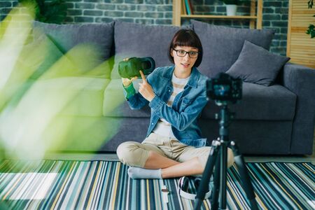 Creative blogger young woman recording video about virtual reality glasses sitting on floor at home holding modern ar device. People and equipment concept.の写真素材