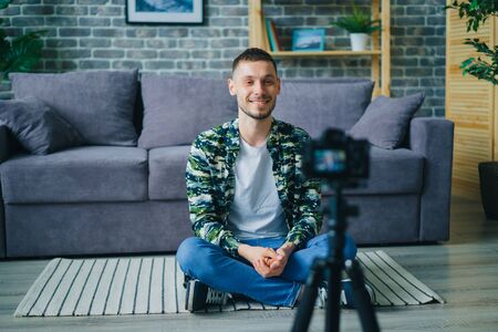 Cheerful young man successful vlogger is recording video for online blog talking looking at professional camera on tripod. Youth and Internet concept.の写真素材
