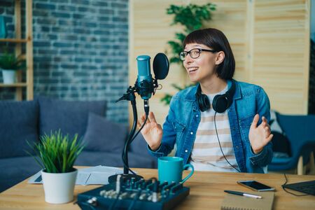 Emotional young woman is speaking gesturing recording audio in microphone at home using modern equipment. People, youth lifestyle and technology concept.の写真素材