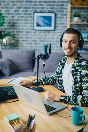Portrait of guy blogger in headphones in recording studio sitting near microphone smiling looking at camera. Blogging, modern technology and people concept.の写真素材