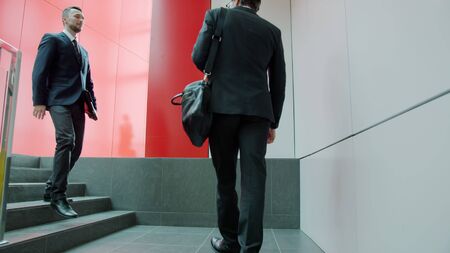 Slow motion of office workers men in suits meeting in hallway shaking hands talking holding to go coffee. Workplace and communication concept.の写真素材