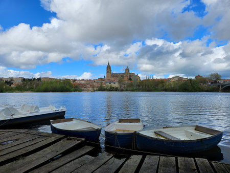 Photograph of a small dock with boats on the banks of the Tormes river, in the distance the complex of Catedrales. Image taken in Salamanca, Castilla y Leon, Spain.の写真素材