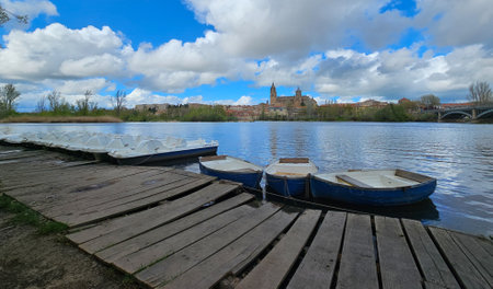 Photograph of several boats on the banks of the Tormes river, in the distance the complex of Catedrales. Image taken in Salamanca, Castilla y Leon, Spain.の写真素材
