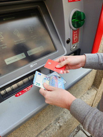 Person operating an ATM, with cash and card in hand in a street in Spain, in a street in Salamanca, Castilla y Leon, Spain, business, banks, money, banknotes, magnetic card, transaction, street, Salamanca, Spainの写真素材