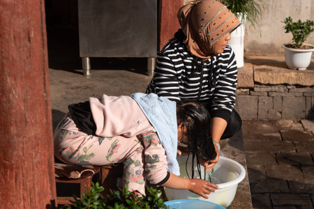 February 2019. Woman washes her daughter's hair. daily life scene in rural village in Yunnan,...