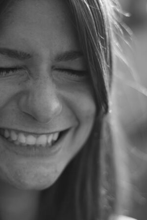 Young woman portrait in black and white. Smiling with tight closed teeth and eyes.の写真素材