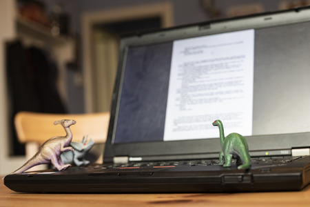 Open laptop on wooden table with small dinosaur toys that seem looking at the screen. Natural light.の写真素材
