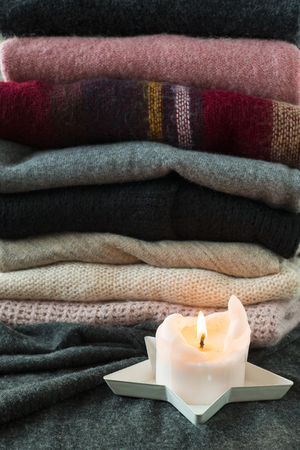 Pile of pink and grey sweaters with glowing candle, cozy winter background or wallpaper. Vertical shot.の写真素材
