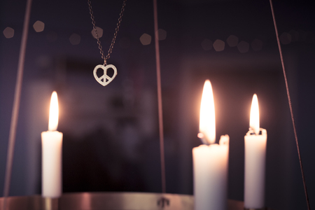 Peace, love, christmas  background with a peace heart symbol pendant hanging among candles glowing on a golden advent chandelier. pink filter.の写真素材