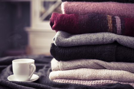 Pile of colorful sweaters with hot drink white cup on the side, background with copy space, cozy hygge wallpaper. Pink filter.の写真素材