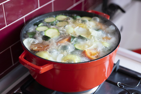 Red pot with boiling vegetable soup on stove, with foam and bubbles. Side view.の写真素材