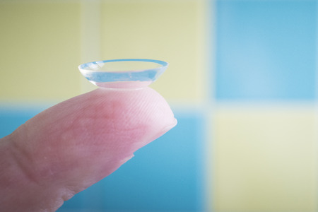 Soft contact lens on finger tip, macro with blue and yellow background and natural light.の写真素材