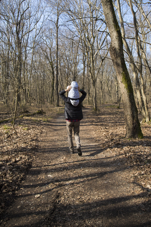 Young dad carrying baby on his shoulders in a forest. Back view, vertical shot.の写真素材