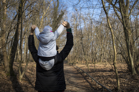 Young dad in a forest, carrying his baby on his shoulders and holding her hands up.の写真素材