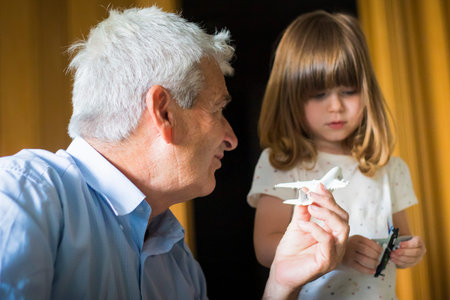 Caucasian grandfather with toddler granddaughter playing with toy aeroplanes in indoor location with...
