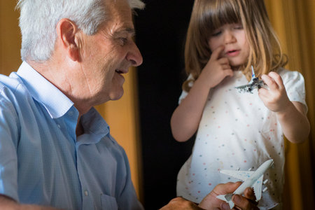 Caucasian grandfather with toddler granddaughter playing with toy aeroplanes in indoor location with natural light.の写真素材