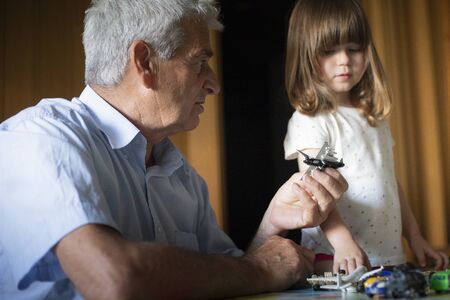 Caucasian grandfather with toddler granddaughter playing with toy aeroplanes in indoor location with natural light.の写真素材