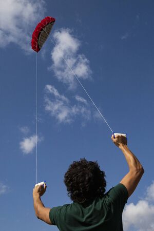 Young man, back view,  controlling a red kite with blue sky in the background. Vertical shot.の写真素材