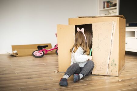 Little child girl sitting in a cardboard playhouse while moving in a new house.の写真素材