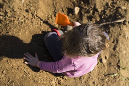 Little child girl digging soil with a scoop in the garden during covid-19 pandemic  lockdown. Outdoor activity idea for children during home staying. Top view, aerial point of view.の写真素材