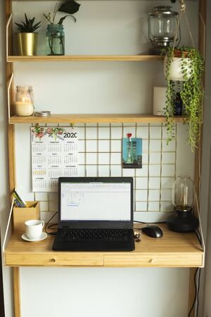Small home office remote station, with laptop, houseplants, metallic board, candles and table lamp. Vertical shot.の写真素材