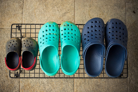Three pairs of colorful rubber gardening sandals or clogs, for each family member, on a rack in the...