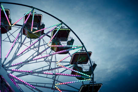 Colorful ferris wheel at dusk, illuminated by neon lights. Background with copy space. Toned, filtered blue color. Rosolina Mare amusement park, Veneto, Italy.の写真素材