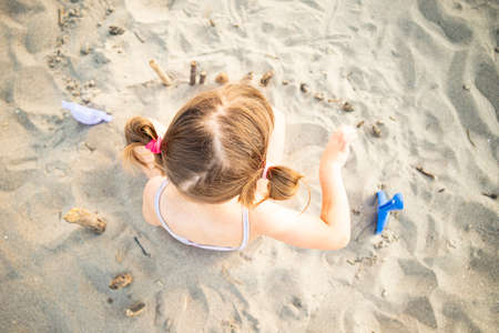 Caucasian child girl playing with sand and driftwoods while sitting on the beach, top view.の写真素材