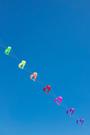 A row of rainbow colored heart shaped kites flying in the blue sky. Background or wallpaper....