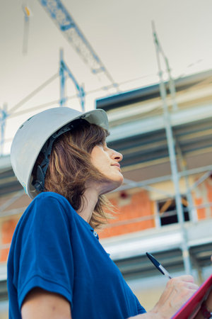 Woman, female engineer, caucasian, age 40, wearing a safety white cap, working on a construction...
