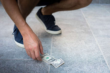 Anonymous man, casual dressed, with blue sneakers, picking up one dollar bill from the ground.の写真素材