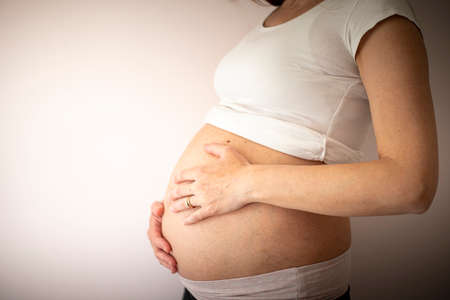 Pregnant woman wearing a white t-shirt with hands on belly on blank background. Profile, side view. Background with copy space.の写真素材