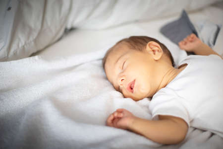 Caucasian newborn sleeping, lying on his back, on white and gray bedding. Copy space.の写真素材