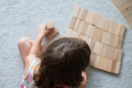 Caucasian child girl, 5 yers old, playing with wooden blocks on the floor, sitting on beige carpet...
