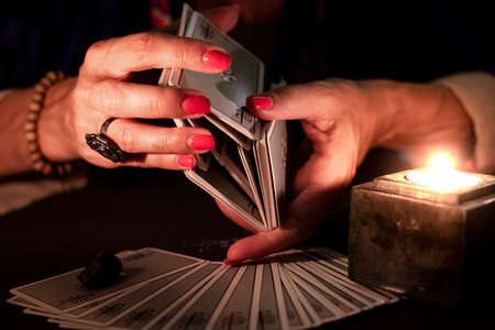 Fortune teller female hands shuffling a deck of tarot cards, during a reading. Close-up with candle light, moody atmosphere.の写真素材