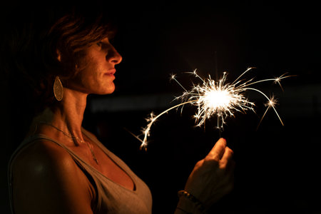 Attractive caucasian woman holding a burning sparkler or bengal in the dark. Profile portrait. Holidays or magic background or wallpaper.の写真素材