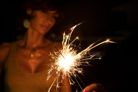 Attractive caucasian woman, blurred face, holding a burning sparkler or bengal in the dark. Copy...